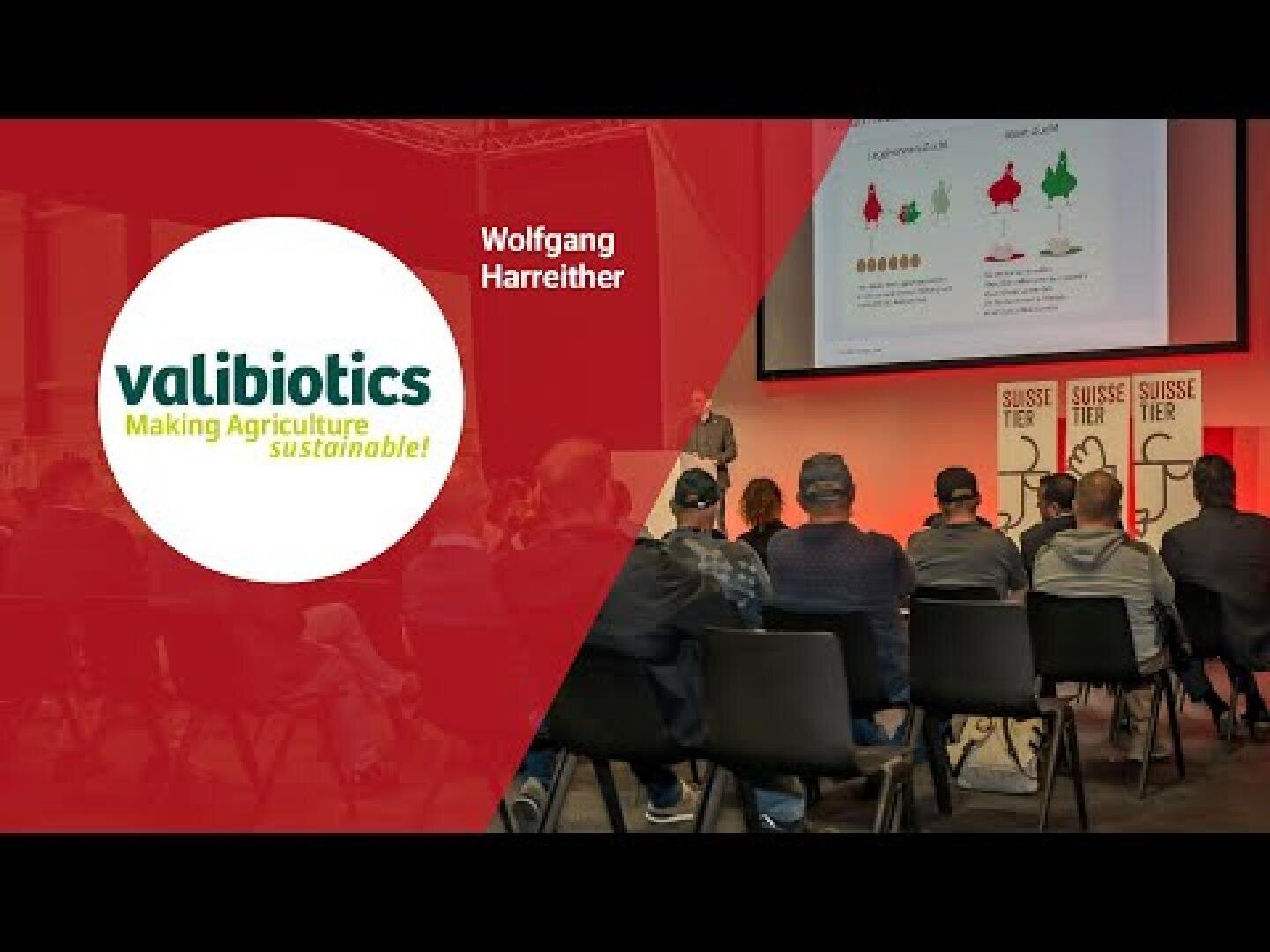 Ein Redner präsentiert dem in Reihen sitzenden Publikum auf einer Bühne eine Folie. Auf dem Bildschirm sind Pflanzengrafiken zu sehen. Auf der linken Seite ist ein rundes Logo mit der Aufschrift valibiotics Making Agriculture sustainable! und darüber der Name Wolfgang Harreither zu sehen.