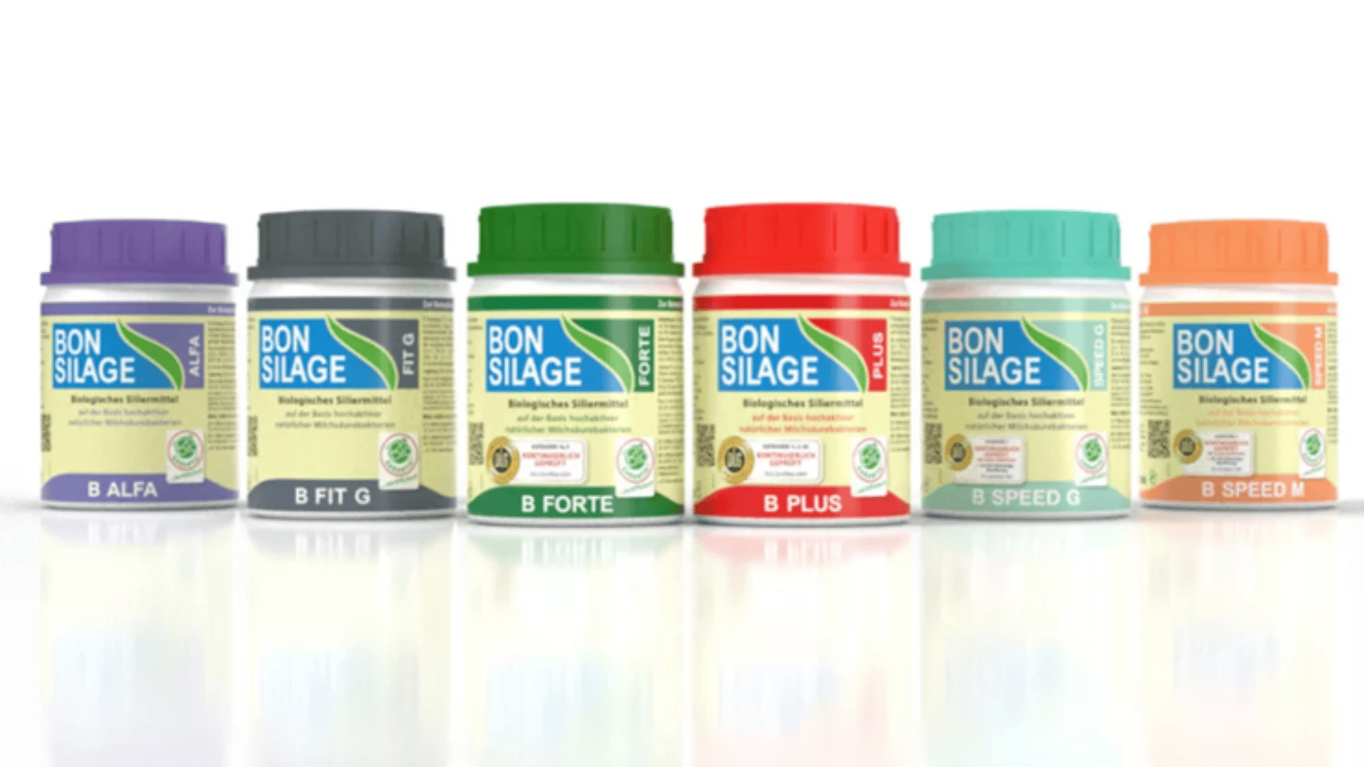 Sechs BON SILAGE Siliermittelbehälter in verschiedenen Farben (violett, grau, grün, rot, türkis und orange) sind nebeneinander auf einer weißen Fläche aufgereiht und mit Etiketten versehen, auf denen die jeweiligen Produktnamen stehen.