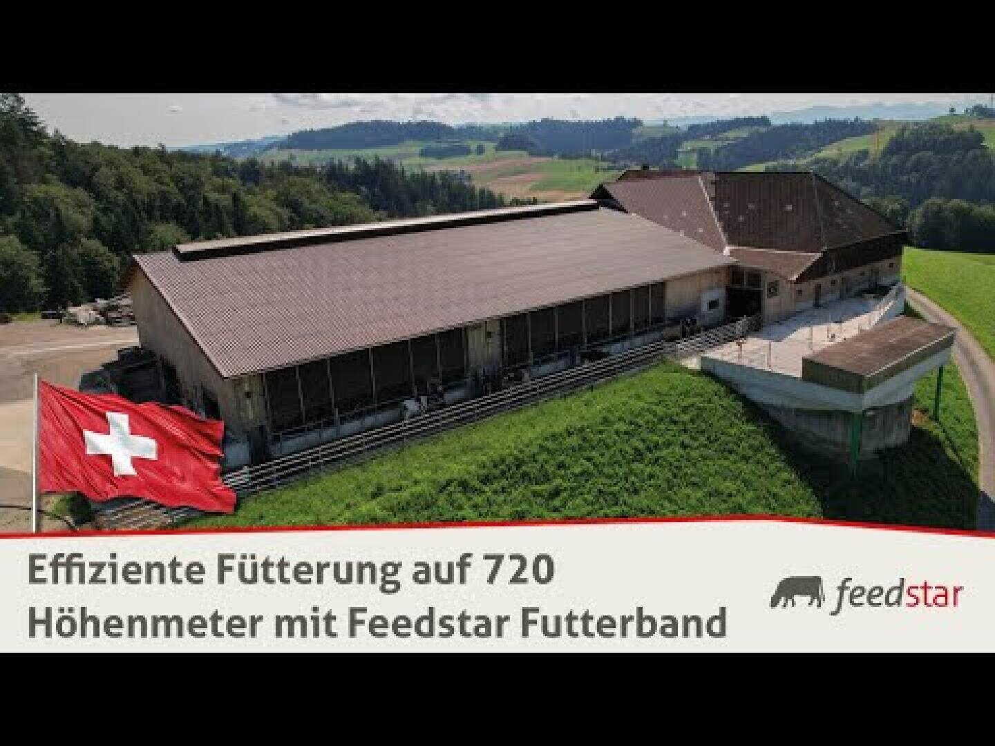 Ein großes landwirtschaftliches Gebäude mit einer Schweizer Fahne im Vordergrund, auf einem grasbewachsenen Hügel mit Feldern und Bäumen im Hintergrund. Der Text lautet: Effiziente Fütterung auf 720 Höhenmetern mit Feedstar Futterband und dem Feedstar-Logo.