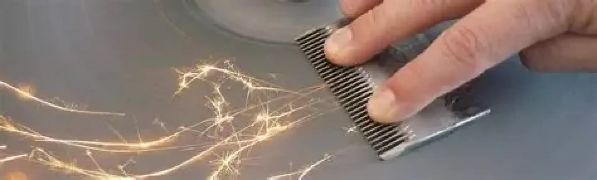 Eine Hand schärft einen Metallkamm auf einer Schleifscheibe, wobei helle Funken entstehen.