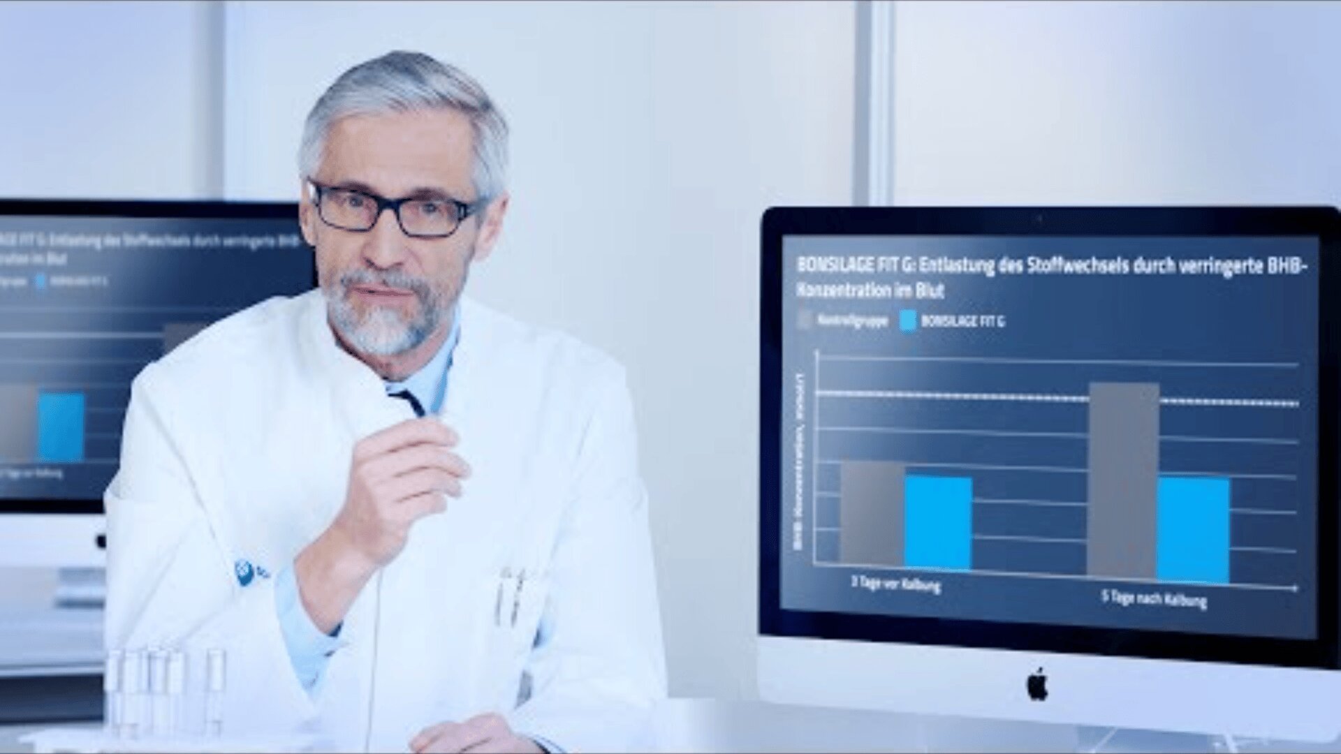 Ein männlicher Arzt in einem weißen Kittel sitzt an einem Schreibtisch und gestikuliert mit seiner Hand. Hinter ihm zeigt ein Computerbildschirm ein Balkendiagramm mit deutschem Text und Daten zum Vergleich der BHB-Konzentration im Blut im Zeitverlauf.
