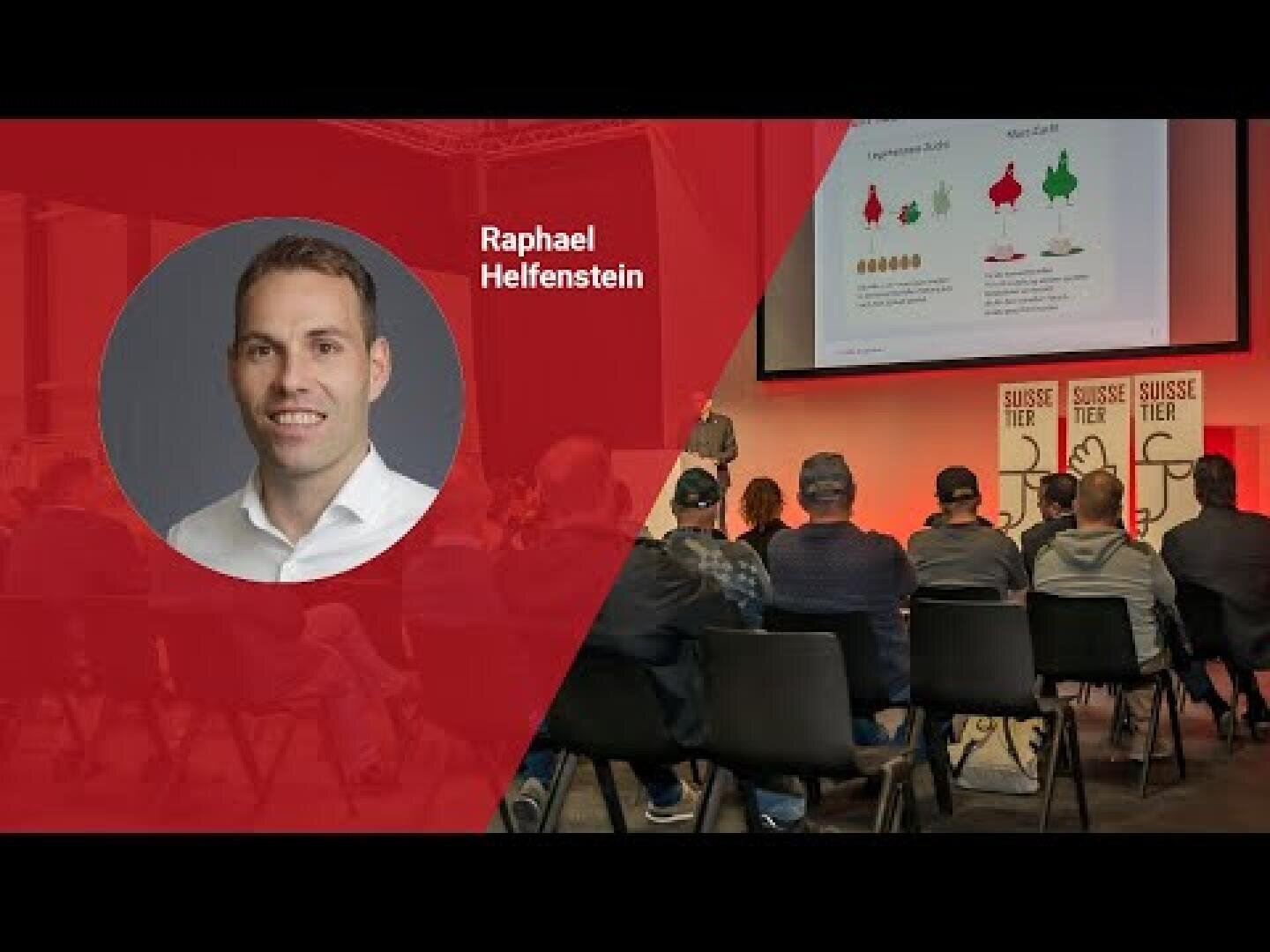 Eine Präsentationsszene mit Personen, die vor einer Bühne und einem Bildschirm sitzen. Auf der linken Seite zeigt eine rote Tafel das Kopfbild eines Mannes mit der Aufschrift Raphael Helfenstein. Auf der Bühne sind Dias und Suisse Tier-Banner zu sehen.