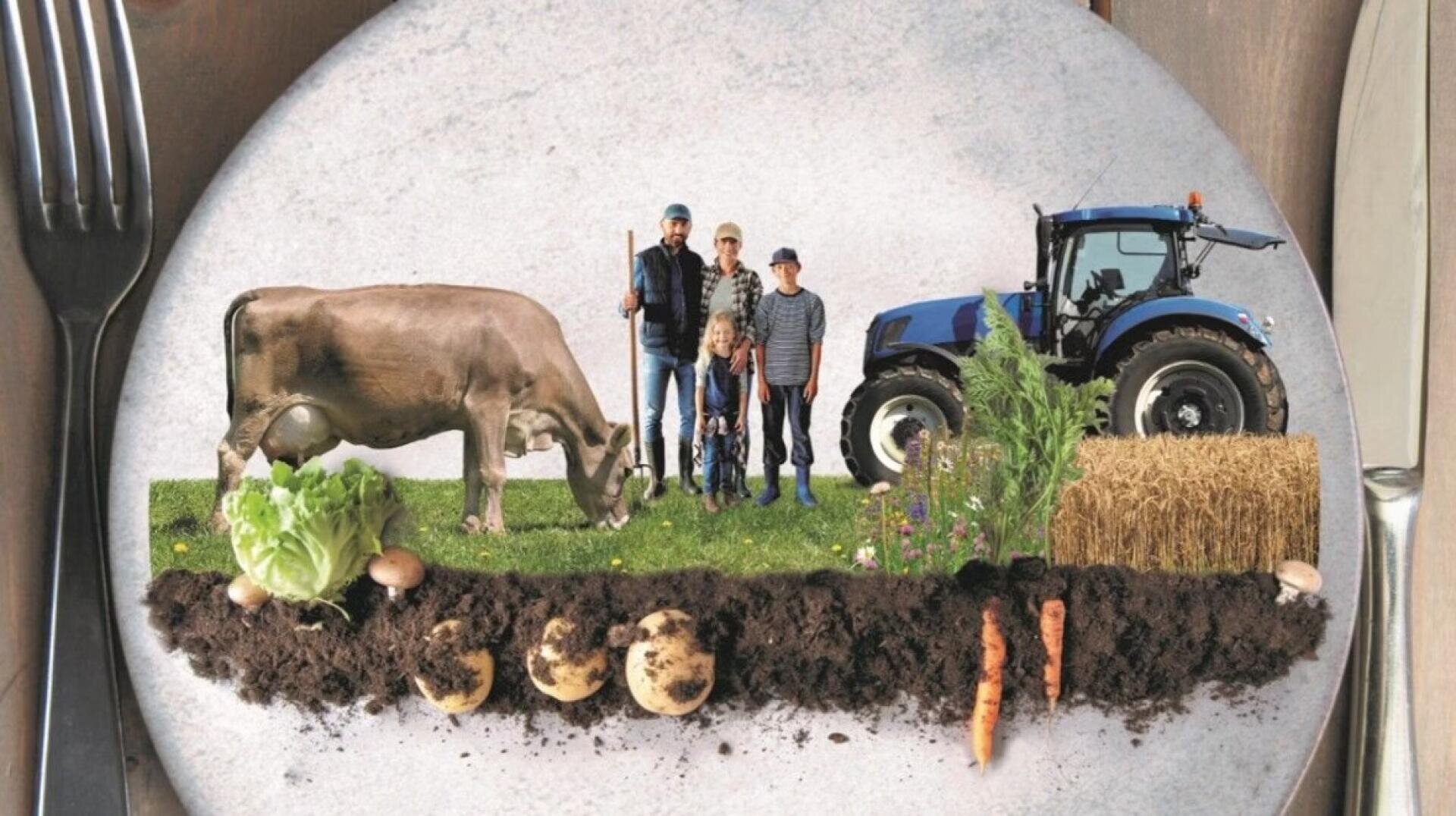 Ein Teller zeigt eine kreative Bauernhofszene mit einer Kuh, einer vierköpfigen Familie, einem blauen Traktor, Heuballen, Gemüse und sichtbaren Bodenschichten, die das Konzept "vom Bauernhof auf den Tisch" symbolisieren. Gabel und Messer sind auf beiden Seiten platziert.