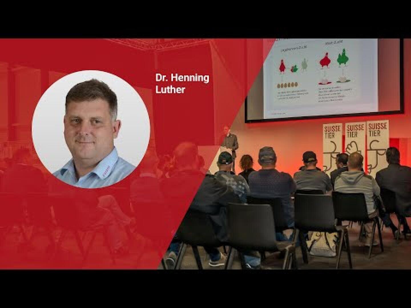 Eine Präsentationsveranstaltung mit einem Publikum vor einer Bühne. Auf einem großen Bildschirm werden Grafiken und der Name Suisse Tier angezeigt. Auf der linken Seite sind Dr. Henning Luthers Foto und Name auf rotem Hintergrund zu sehen.