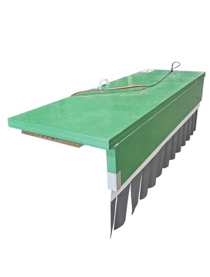 Eine große, rechteckige, grüne Industriemaschine mit einer flachen Oberseite, elektrischen Leitungen auf der Oberfläche und schwarzen, flexiblen Klappen, die von einer Seite herabhängen.