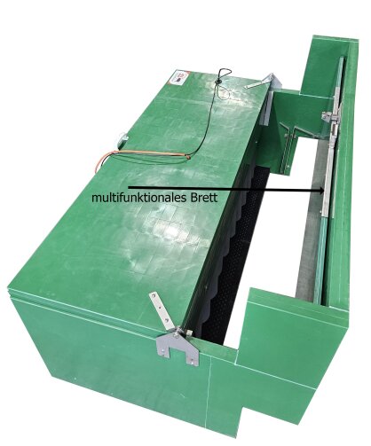 Ein großes, grünes, rechteckiges Gerät mit einem offenen Deckel, Metallscharnieren, Kabeln und einem mit einem Pfeil gekennzeichneten Abschnitt, der als multifunktionales Brett bezeichnet wird.