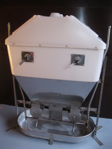 Ein Futterautomat aus weißem und rostfreiem Stahl mit einem schrägen Behälter, zwei Hebelspendern vorne und einer Schale unten zum Auffangen des Futters. Das Gerät steht auf einer ebenen Fläche.