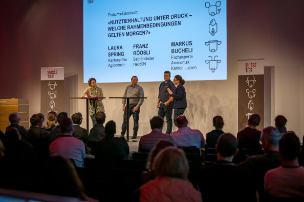 Vier Personen stehen während einer Podiumsdiskussion an der Suisse Tier 2023 auf der Bühne. Auf einer grossen Leinwand hinter ihnen werden die Namen und Titel der Podiumsteilnehmer angezeigt, während das Publikum im Vordergrund zuschaut.