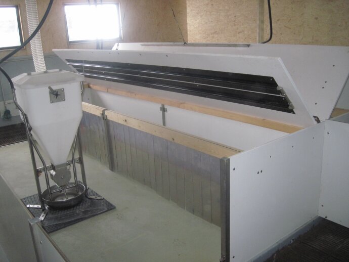 Eine große, weiße, industrielle Tierfütterungsstation mit einer Metallfütterung und einem abgetrennten Gehege in einem Reinraum mit hellen Wänden und Fenstern.