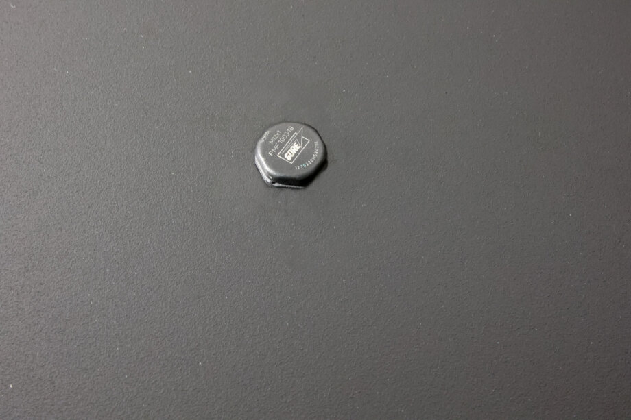 Eine einzelne Sechskantschraube mit der Aufschrift FURNITURE FIXER wird in eine flache, dunkelgraue, strukturierte Oberfläche geschraubt.