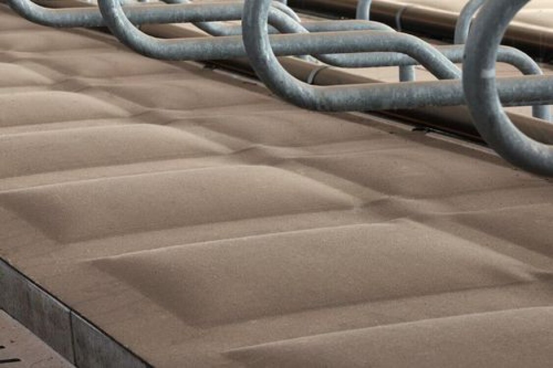 Nahaufnahme von weichen, braunen, rechteckigen Einstreupolstern, die in Reihen unter Metallstäben angeordnet sind und normalerweise als Kuhbetten in einem Milchviehstall verwendet werden.